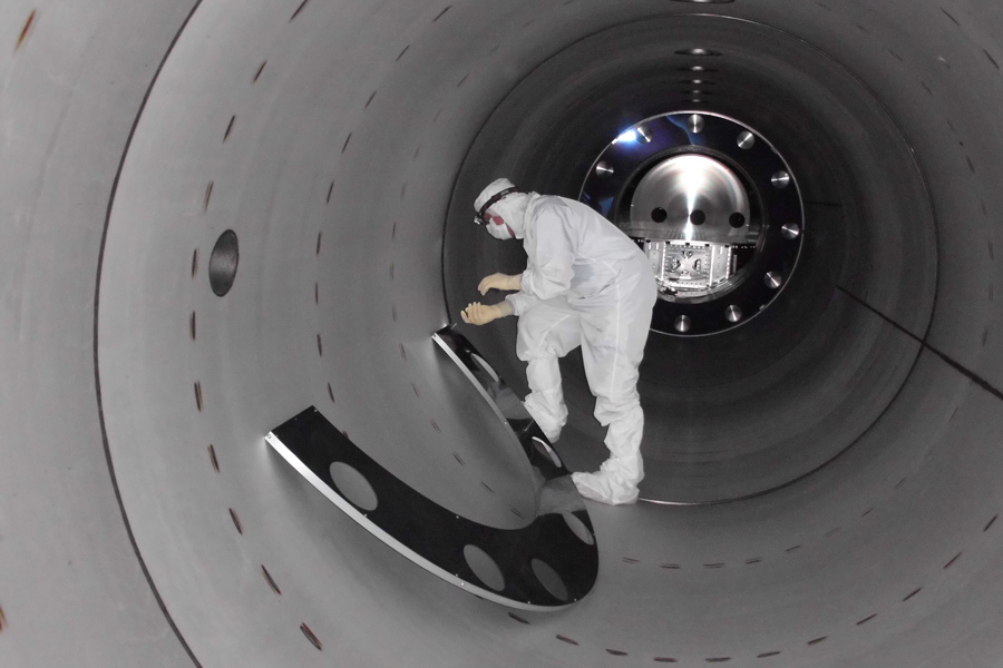 Worker in a cleanroom suit installing baffles inside the LIGO vacuum tube